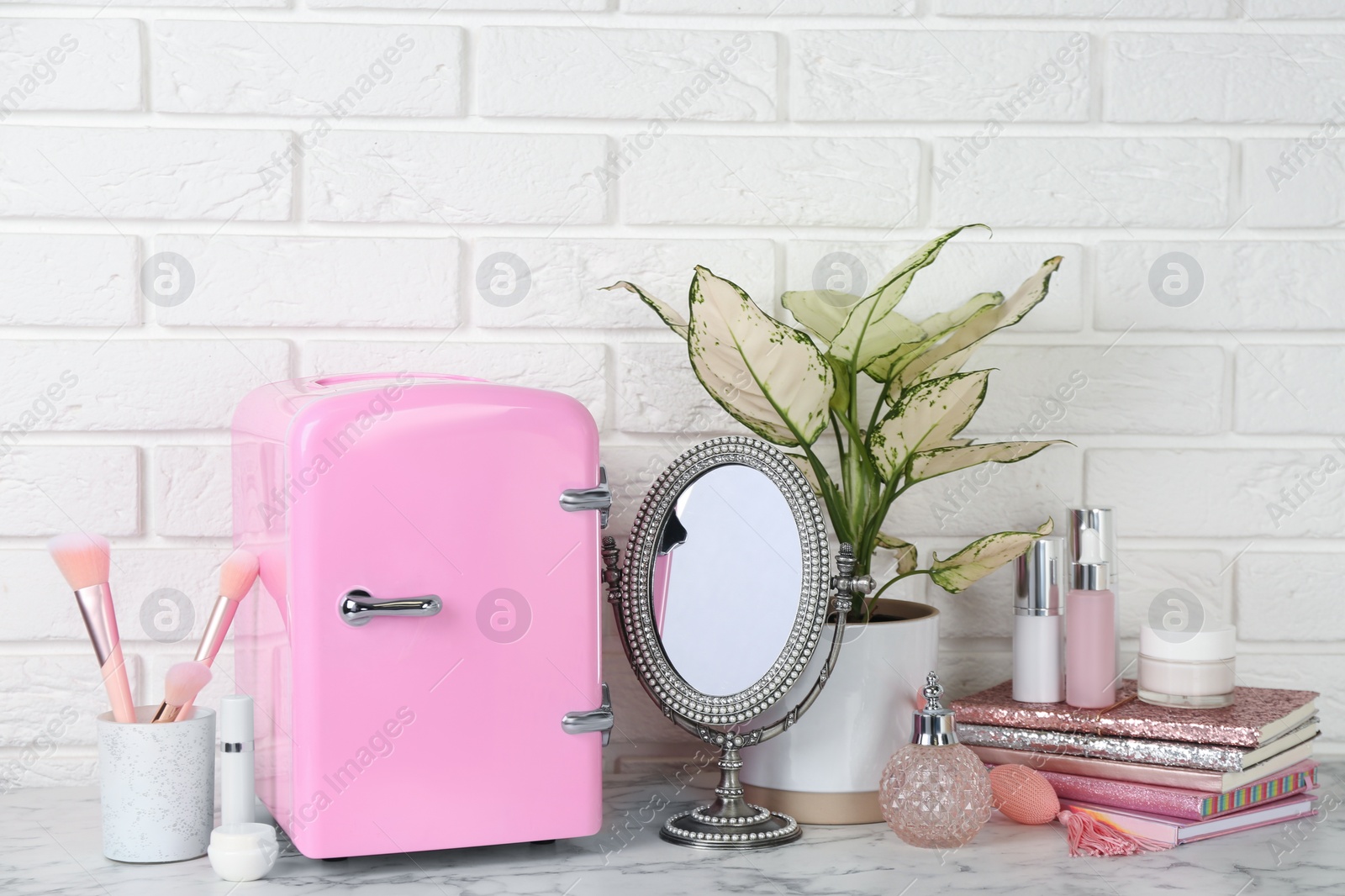 Photo of Cosmetic refrigerator and skin care products on white marble table