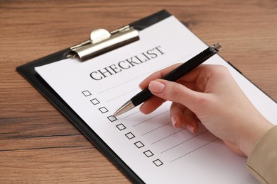 Woman filling Checklist at wooden table, closeup