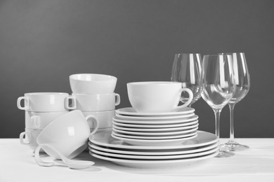 Set of clean dishware and glasses on white wooden table against grey background