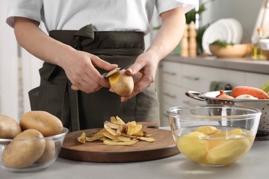 Photo of Woman peeling fresh potato with knife at light table indoors, closeup