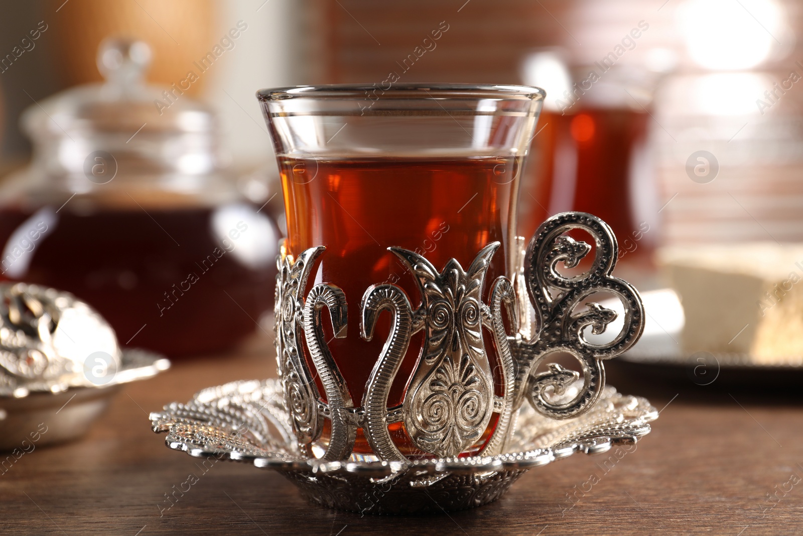 Photo of Glass of traditional Turkish tea in vintage holder on wooden table, closeup