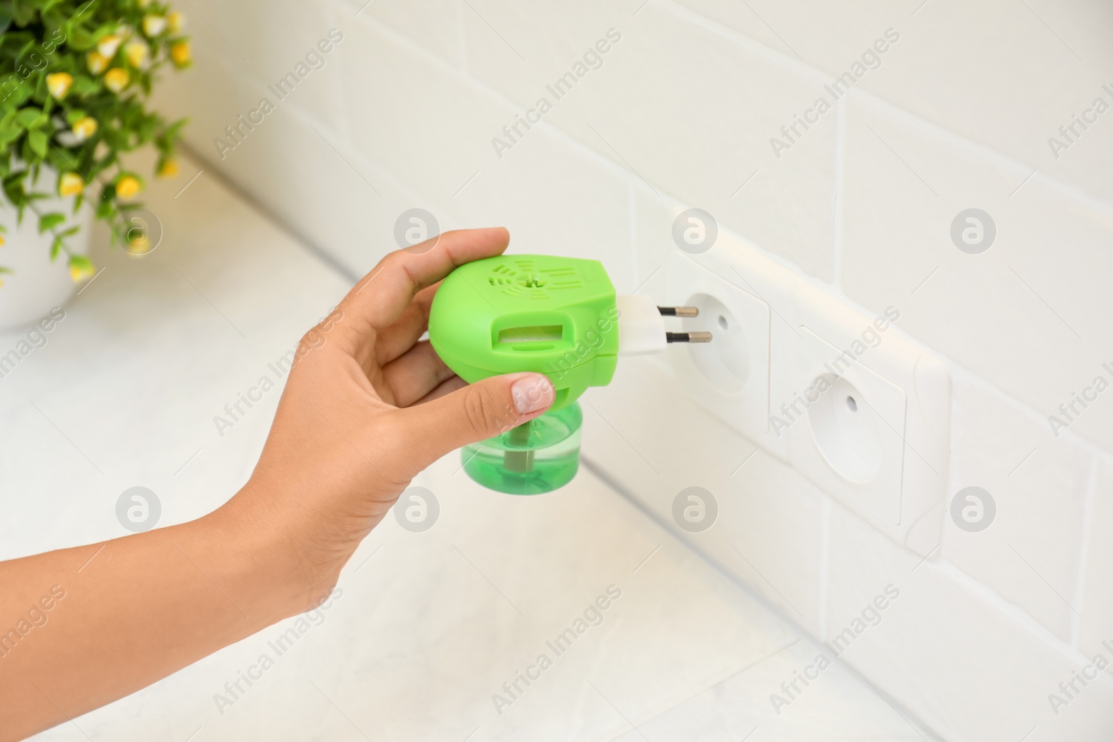 Photo of Woman plugging electric vaporizer with insect repellent liquid at home, closeup