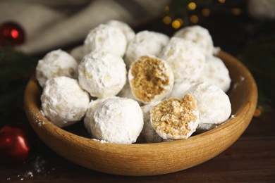 Photo of Tasty snowball cookies in wooden bowl on table, closeup. Christmas treat