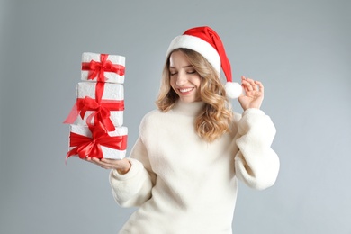 Beautiful young woman in Santa hat with Christmas presents on light grey background