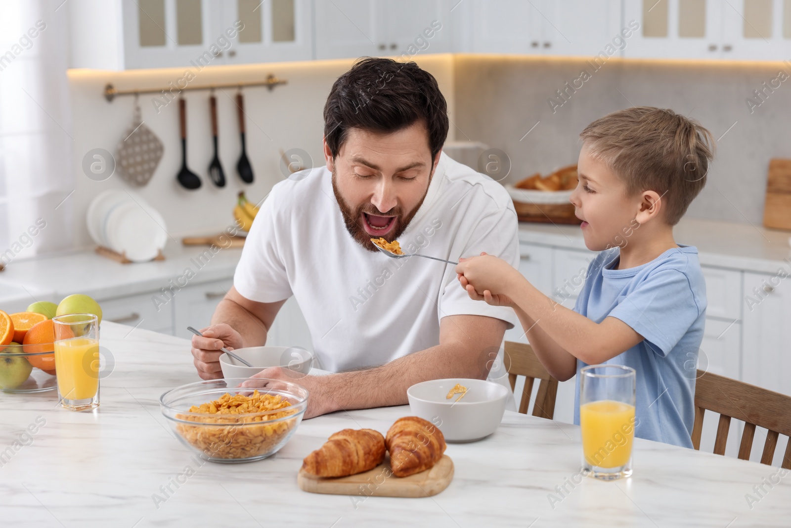 Photo of Father and his cute little son having breakfast at table in kitchen