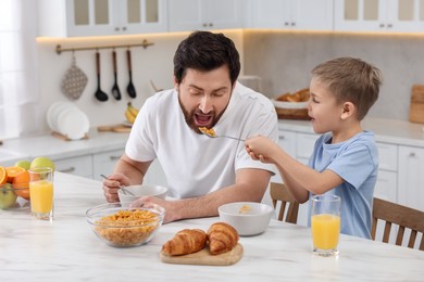 Father and his cute little son having breakfast at table in kitchen