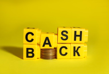 Photo of Word Cashback made with cubes and coins on yellow background, closeup