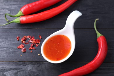 Photo of Spicy chili sauce in spoon and peppers on black wooden table