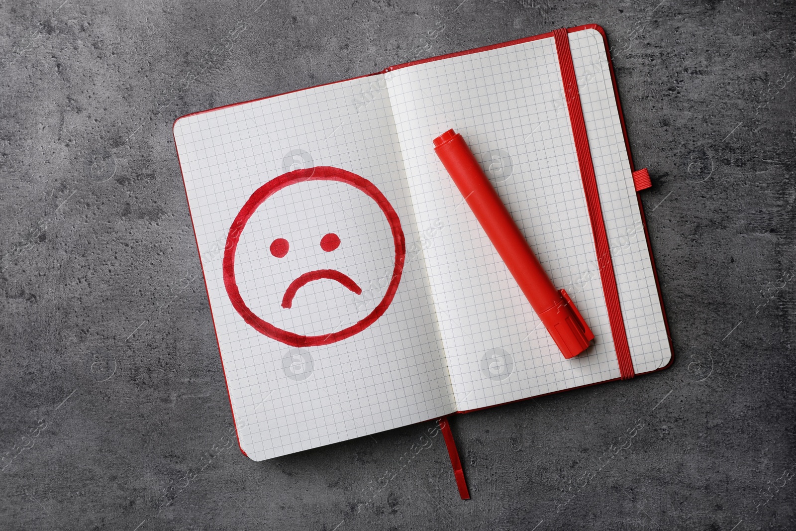 Photo of Notebook with drawing of unhappy face and red marker on grey background, top view. Depression symptoms