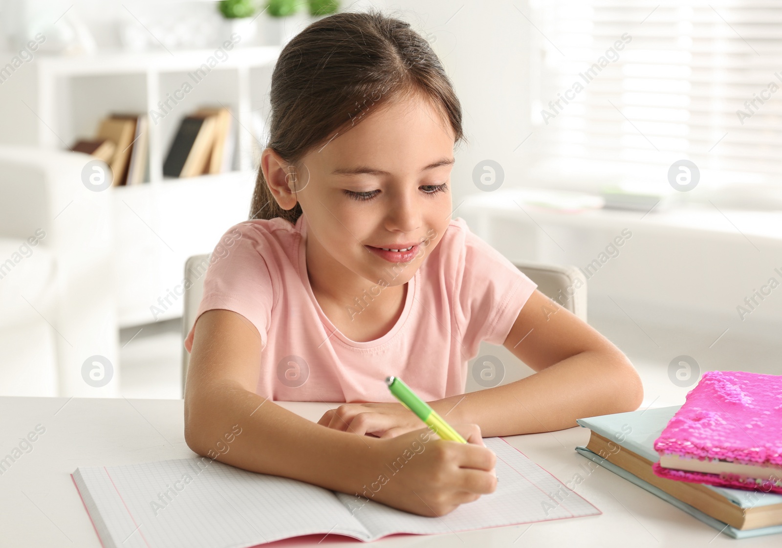 Photo of Little girl doing homework at table indoors