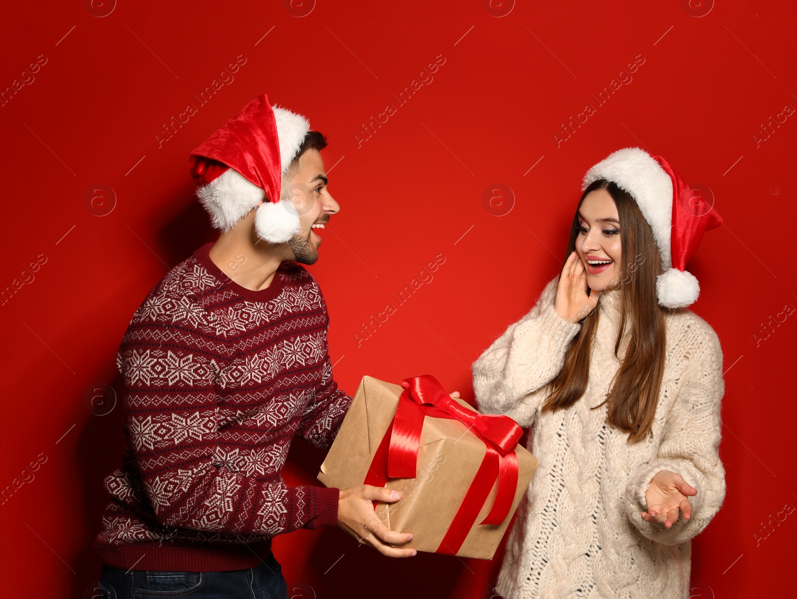 Photo of Couple wearing Christmas sweaters and Santa hats on red background