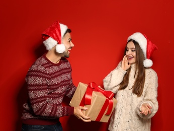 Couple wearing Christmas sweaters and Santa hats on red background