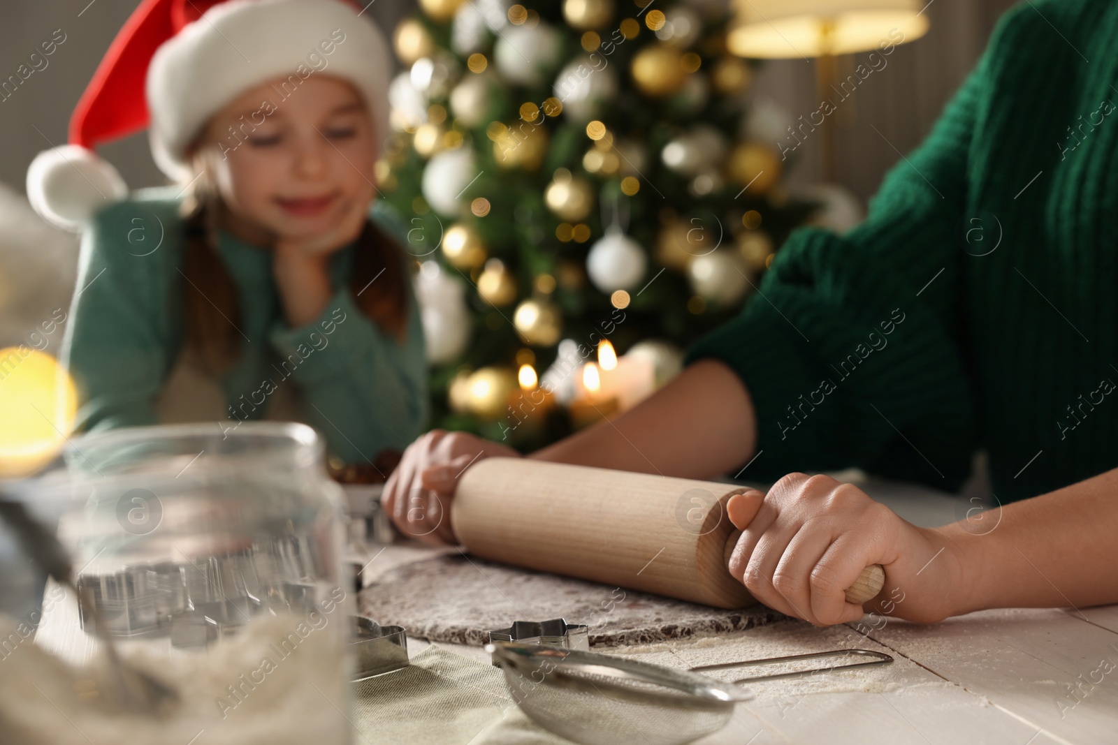 Photo of Mother teaching her daughter how to make Christmas cookies at table indoors, closeup