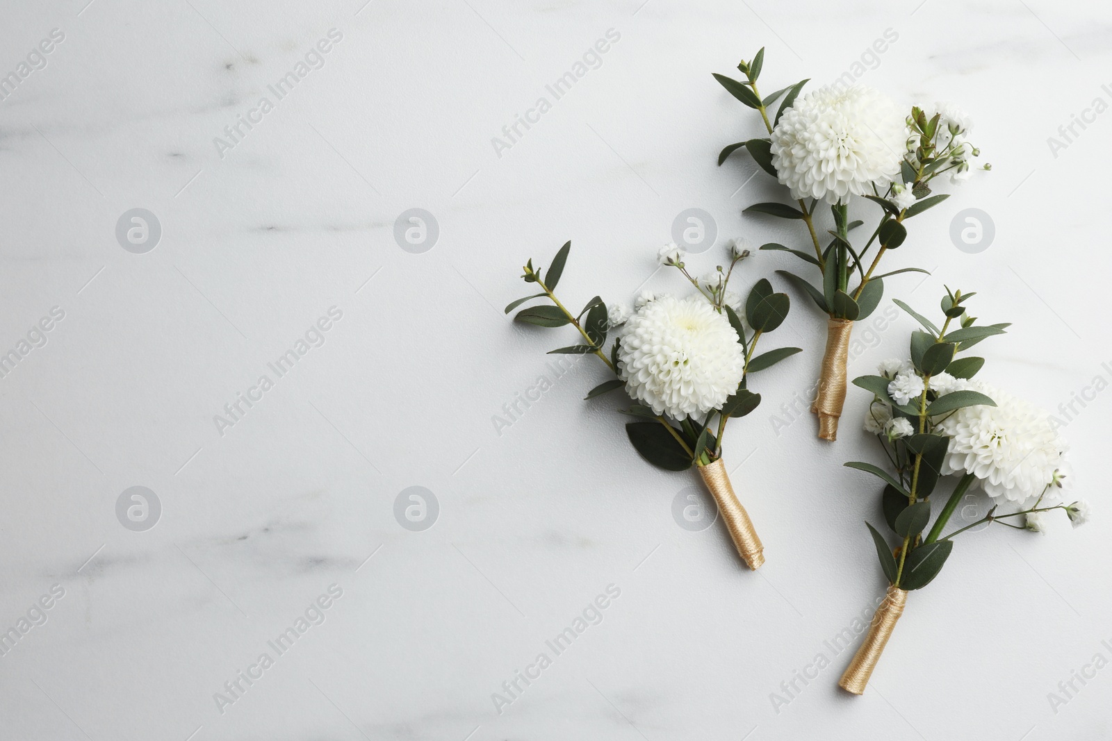 Photo of Small stylish boutonnieres on white marble table, flat lay. Space for text