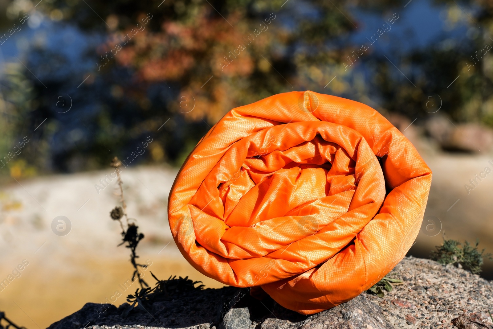 Photo of Orange sleeping bag on rock outdoors, space for text. Camping equipment