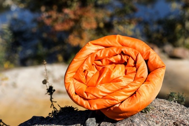 Photo of Orange sleeping bag on rock outdoors, space for text. Camping equipment