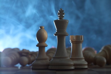 Photo of Wooden king, rook and bishop in front of fallen chess pieces on checkerboard against blue background, closeup
