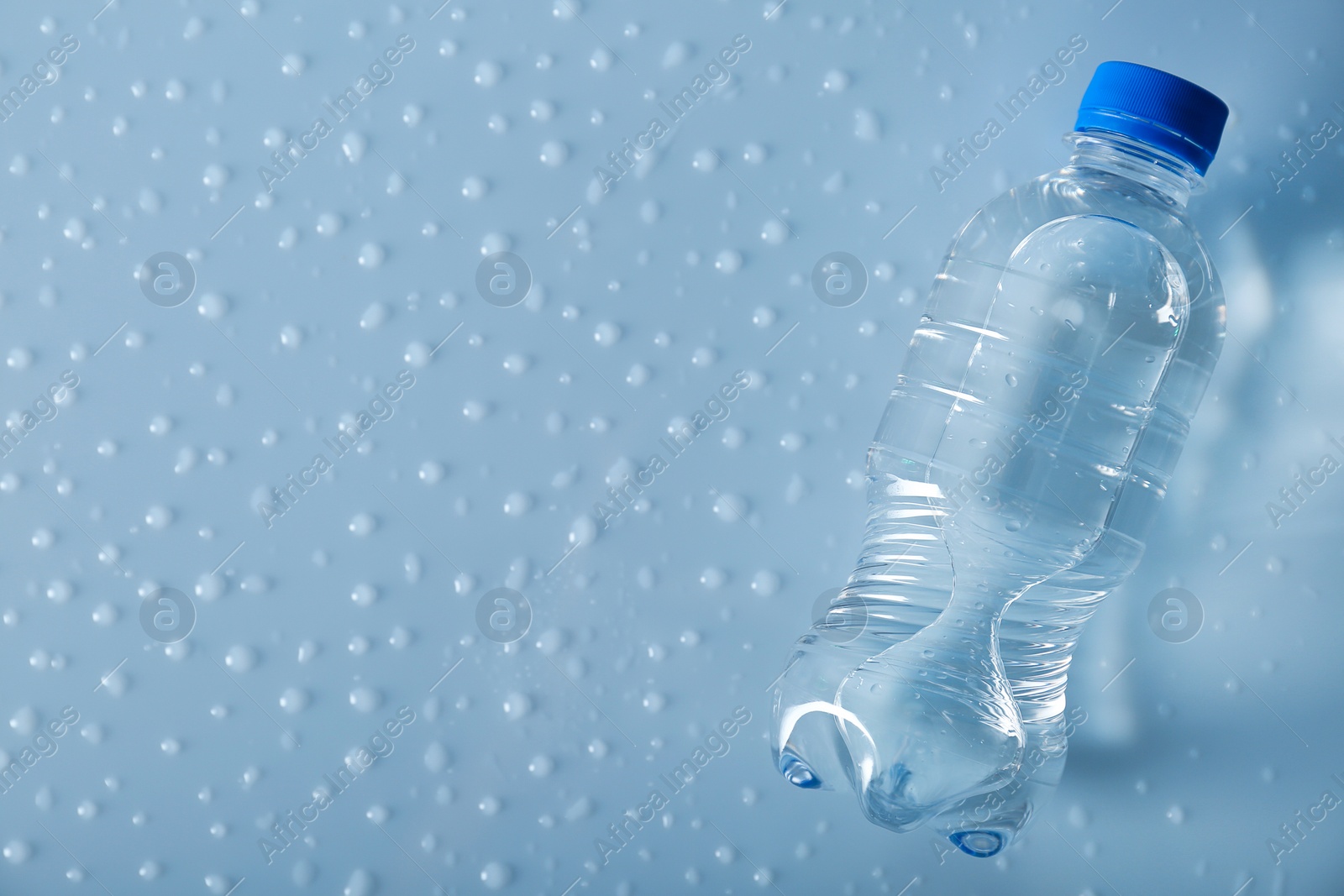 Photo of Bottle of water on wet light surface, top view. Space for text