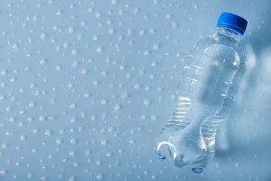 Photo of Bottle of water on wet light surface, top view. Space for text