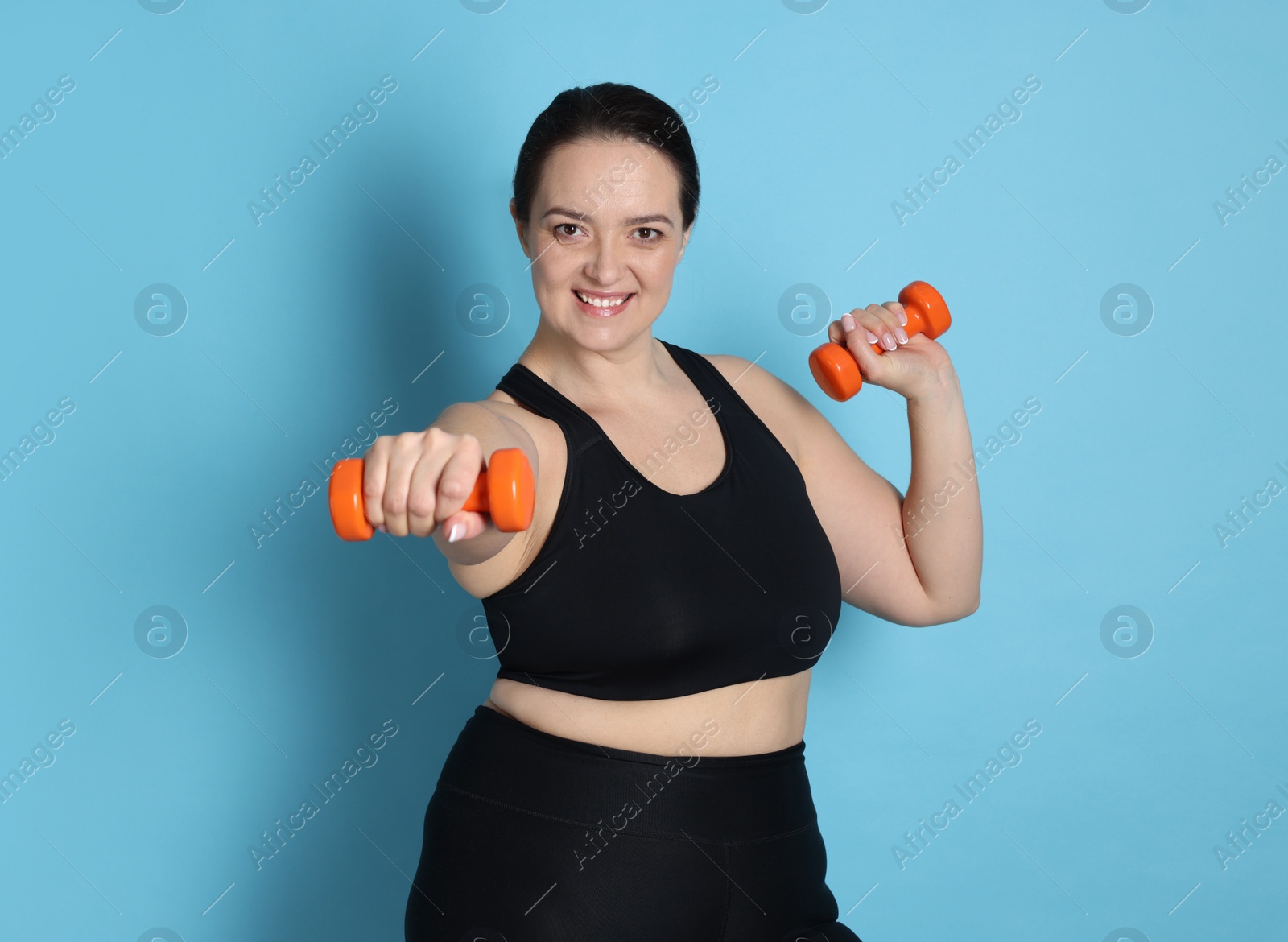 Photo of Happy overweight woman doing exercise with dumbbells on light blue background