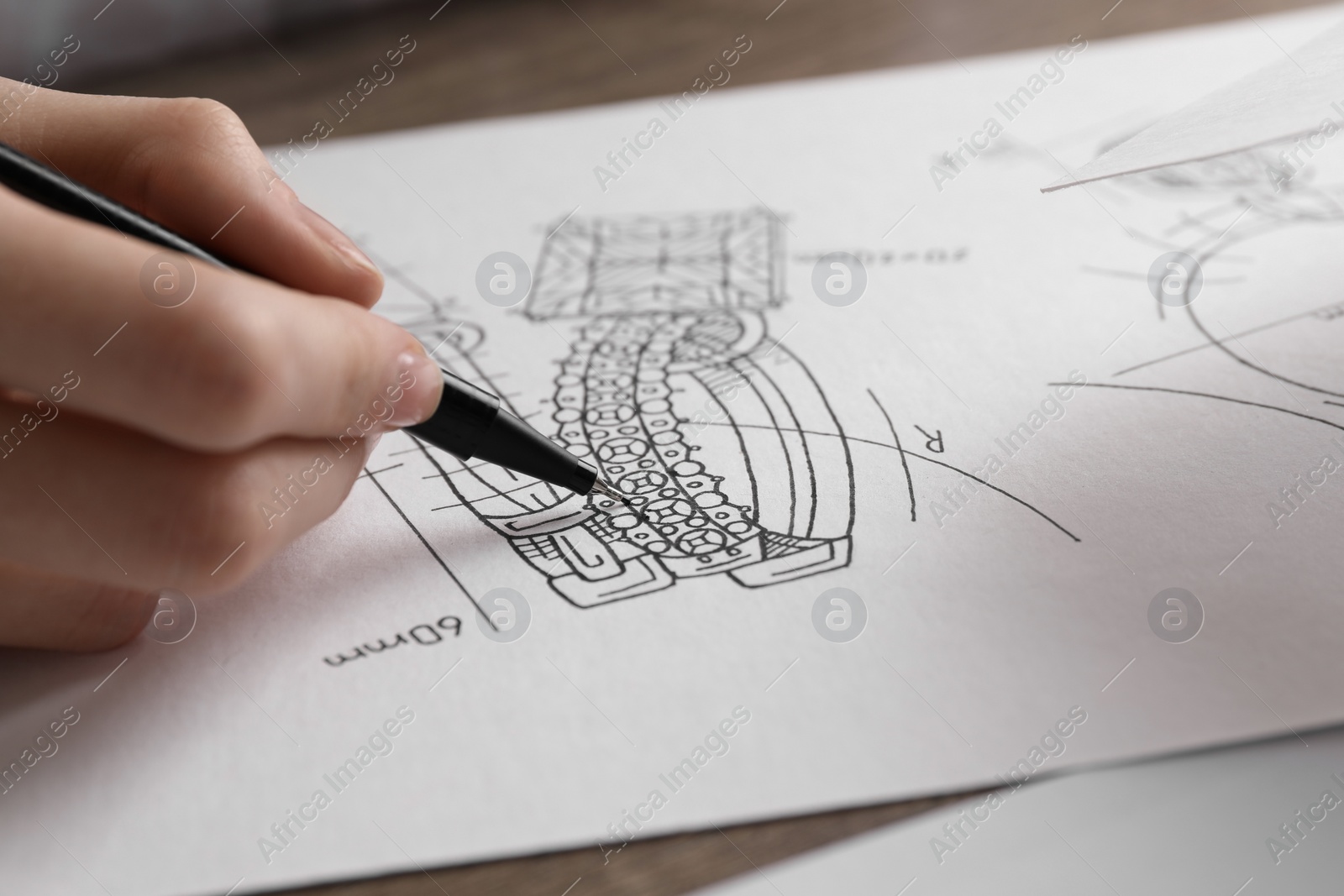 Photo of Jeweler drawing sketch of elegant earrings at wooden table, closeup