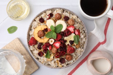Photo of Oatmeal with freeze dried fruits, nuts and mint on white tiled table, flat lay
