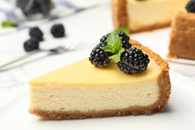 Piece of delicious cheesecake decorated with blackberries on table