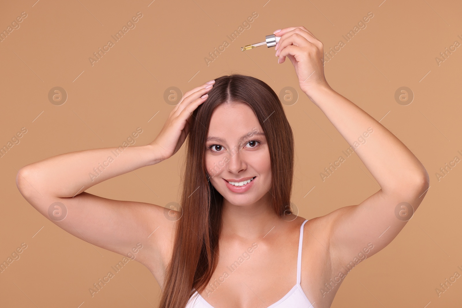 Photo of Beautiful woman applying serum onto hair on beige background