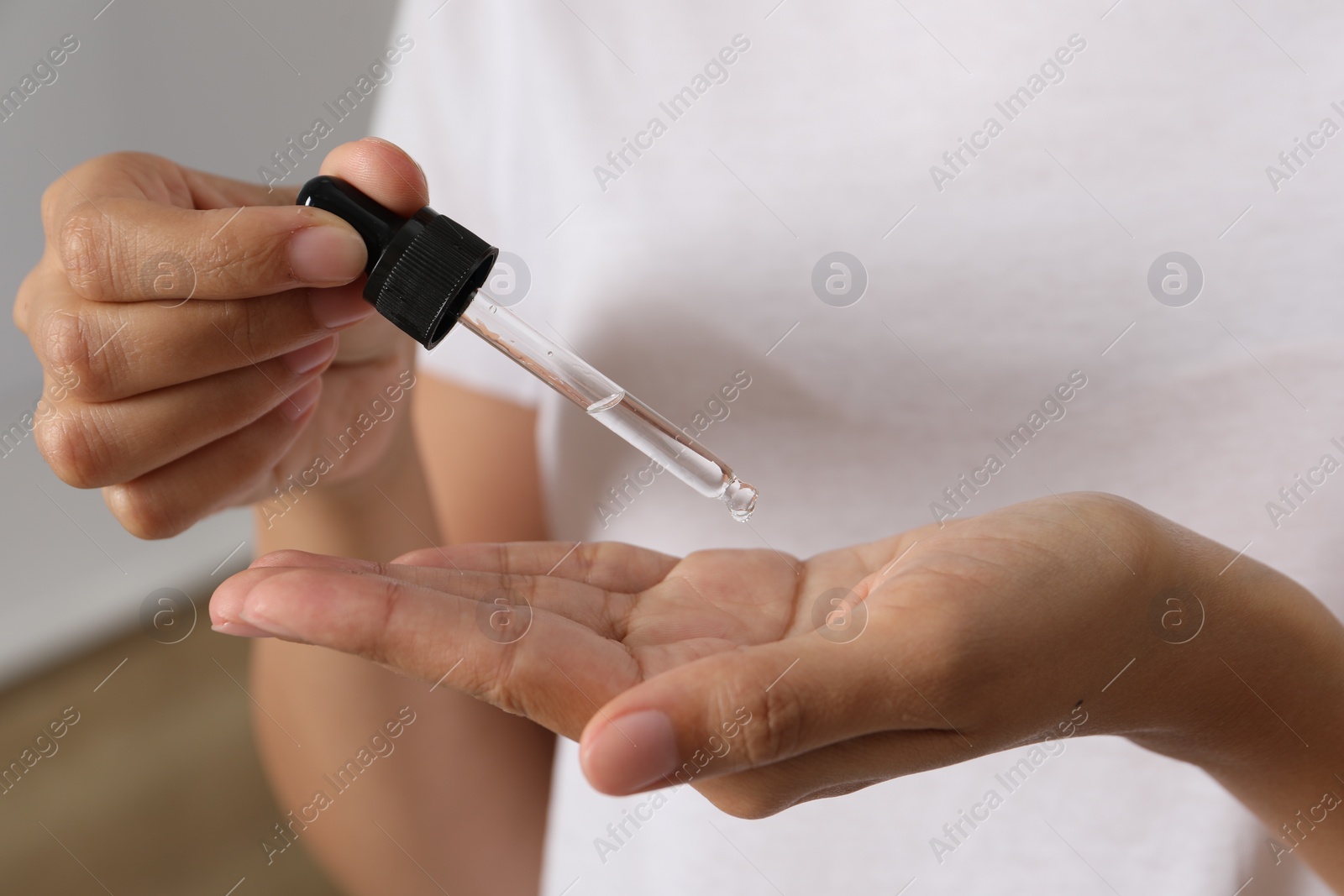 Photo of Woman applying cosmetic serum onto her hand on blurred background, closeup