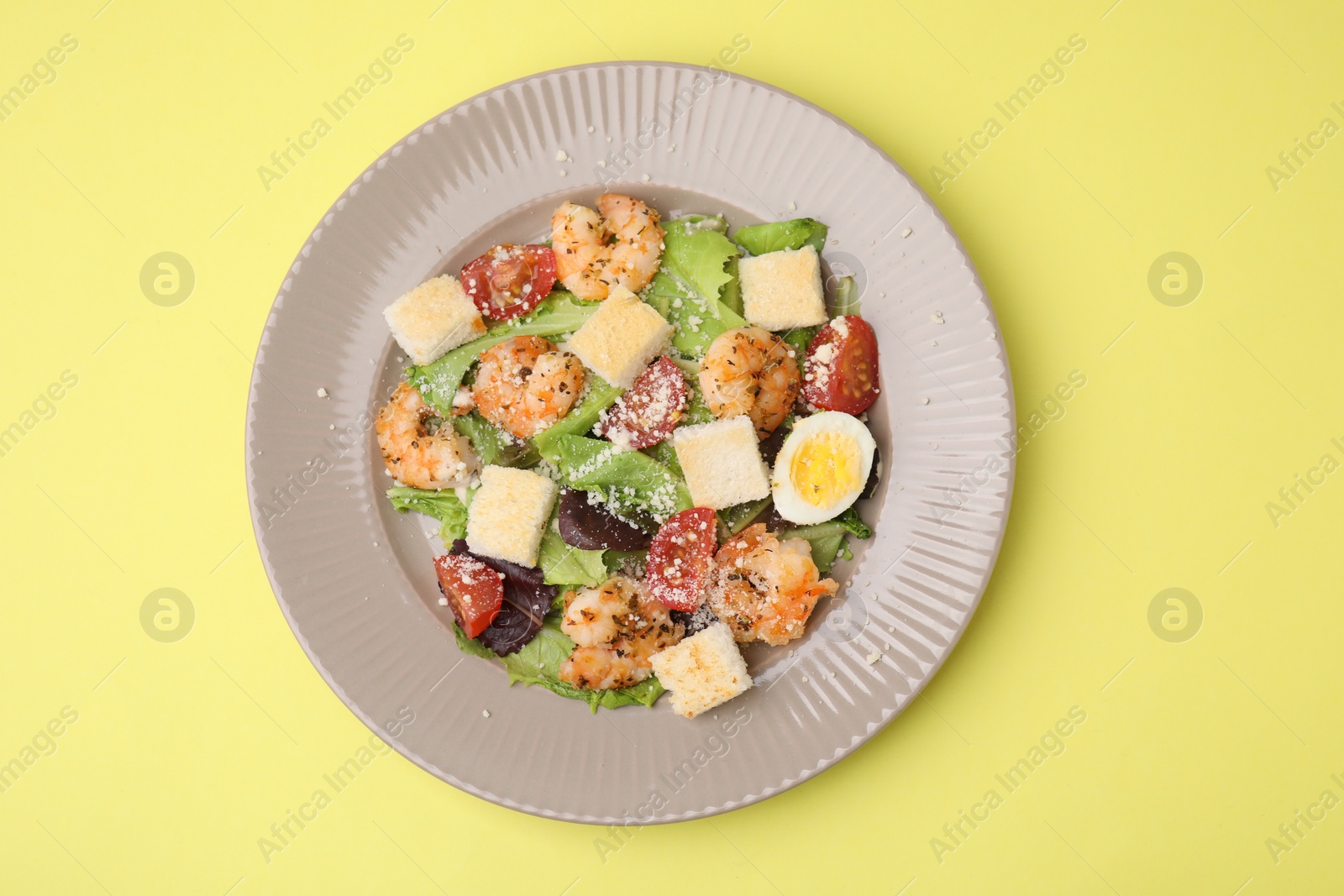 Photo of Delicious Caesar salad with shrimps on yellow background, top view