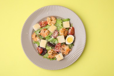 Delicious Caesar salad with shrimps on yellow background, top view