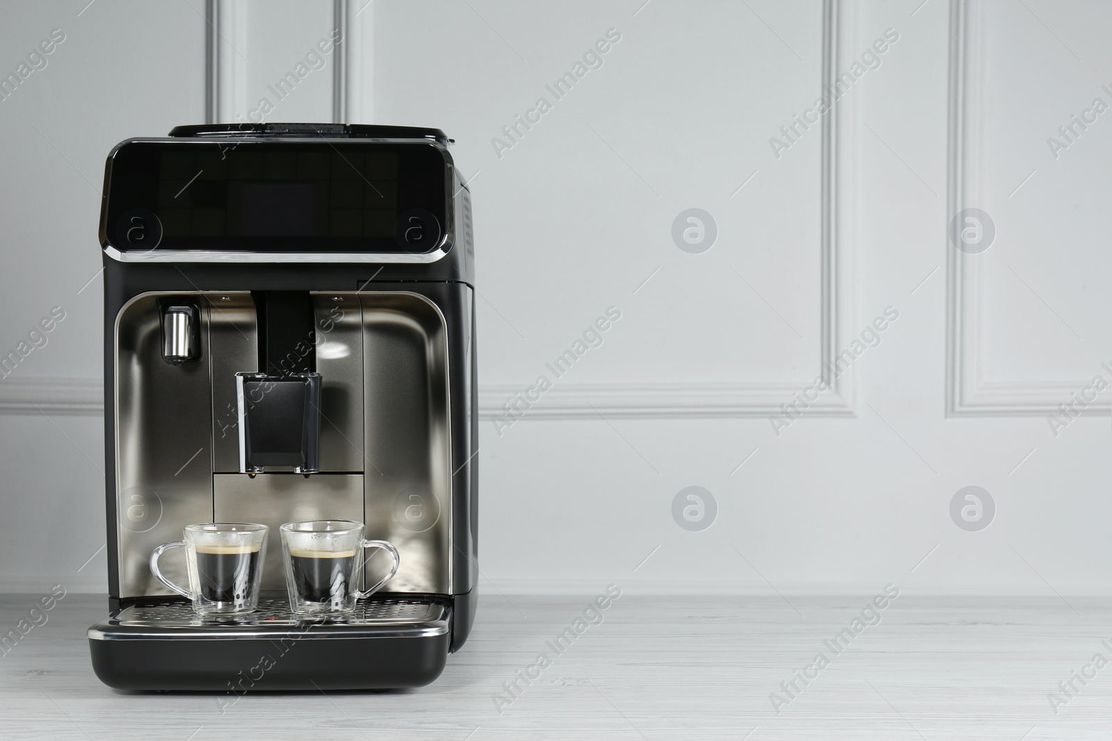 Photo of Modern espresso machine with cups of coffee on white wooden table near light wall. Space for text