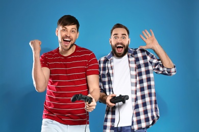 Photo of Emotional men playing video games with controllers on color background