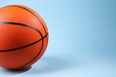 Photo of One orange basketball ball on light blue background, closeup. Space for text