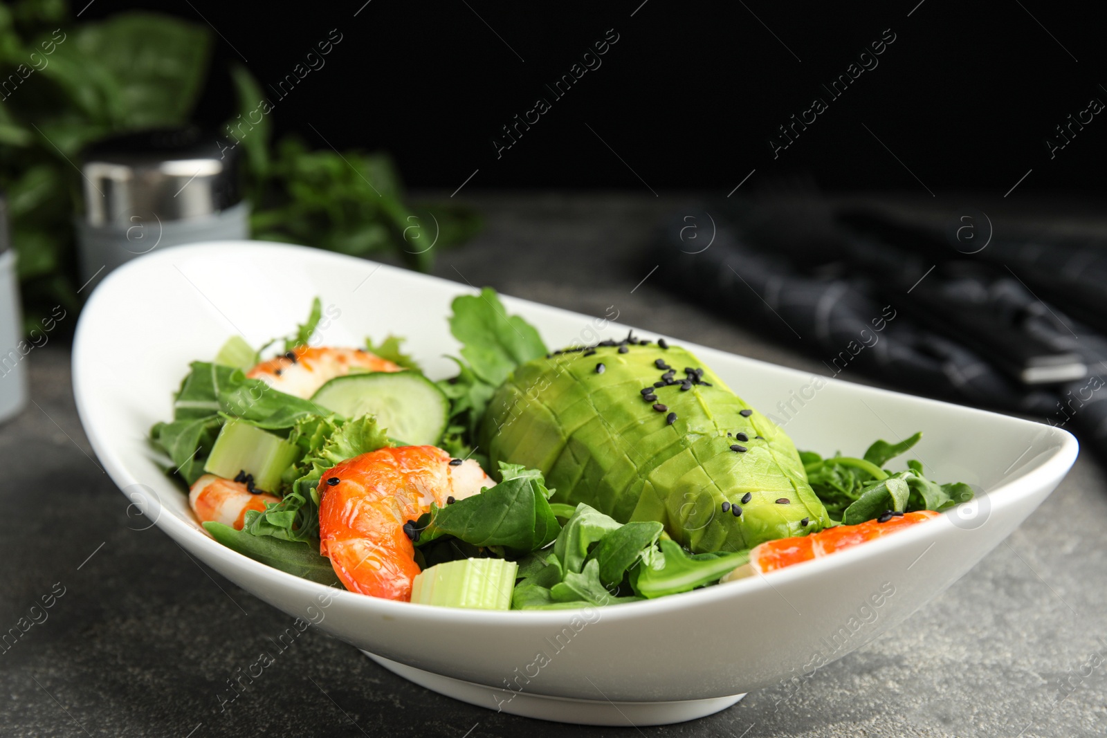 Photo of Delicious avocado salad with shrimps in bowl on grey table