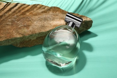 Photo of Bottle of luxury perfume in sunlight and stone on turquoise background