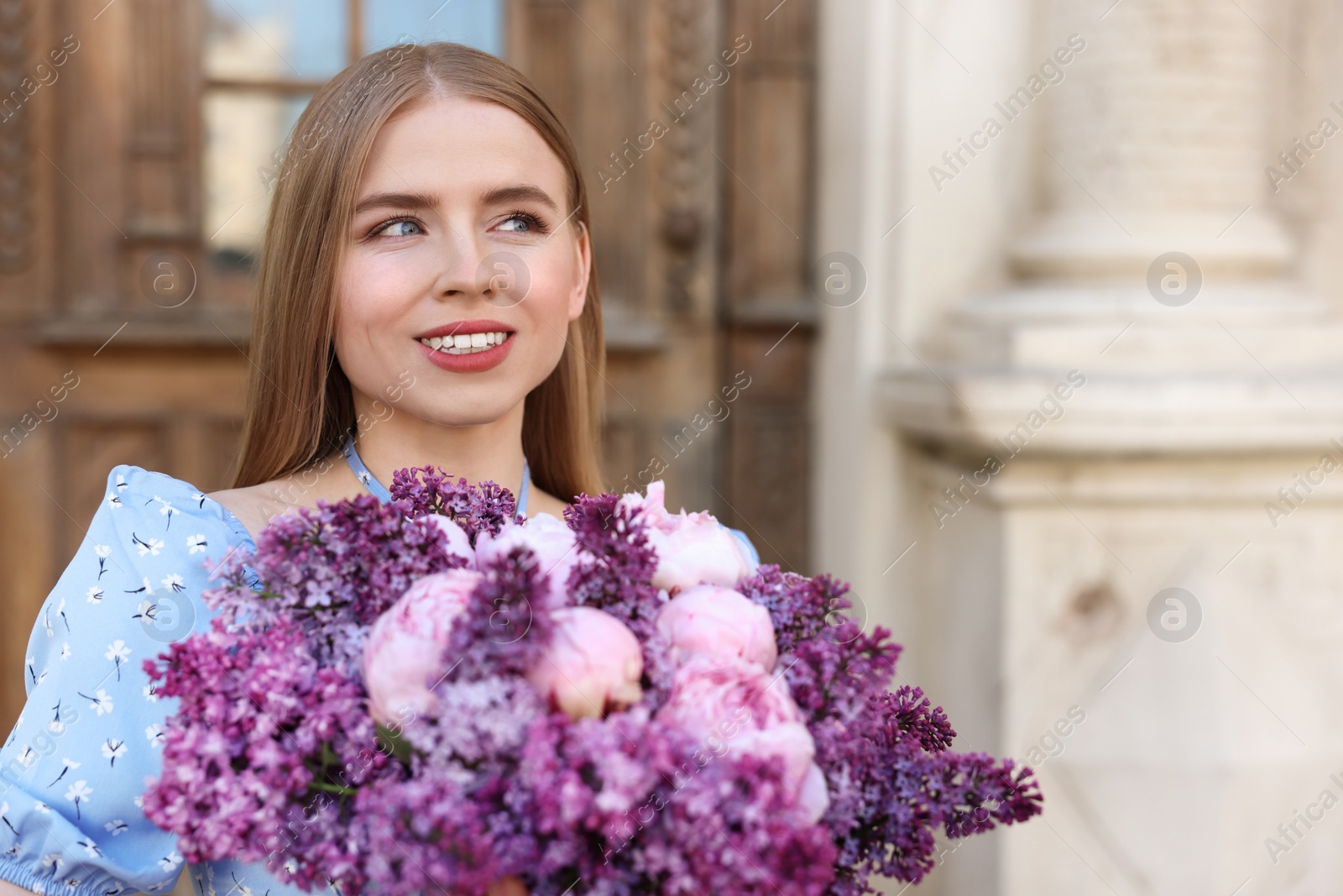 Photo of Beautiful woman with bouquet of spring flowers near building outdoors, space for text