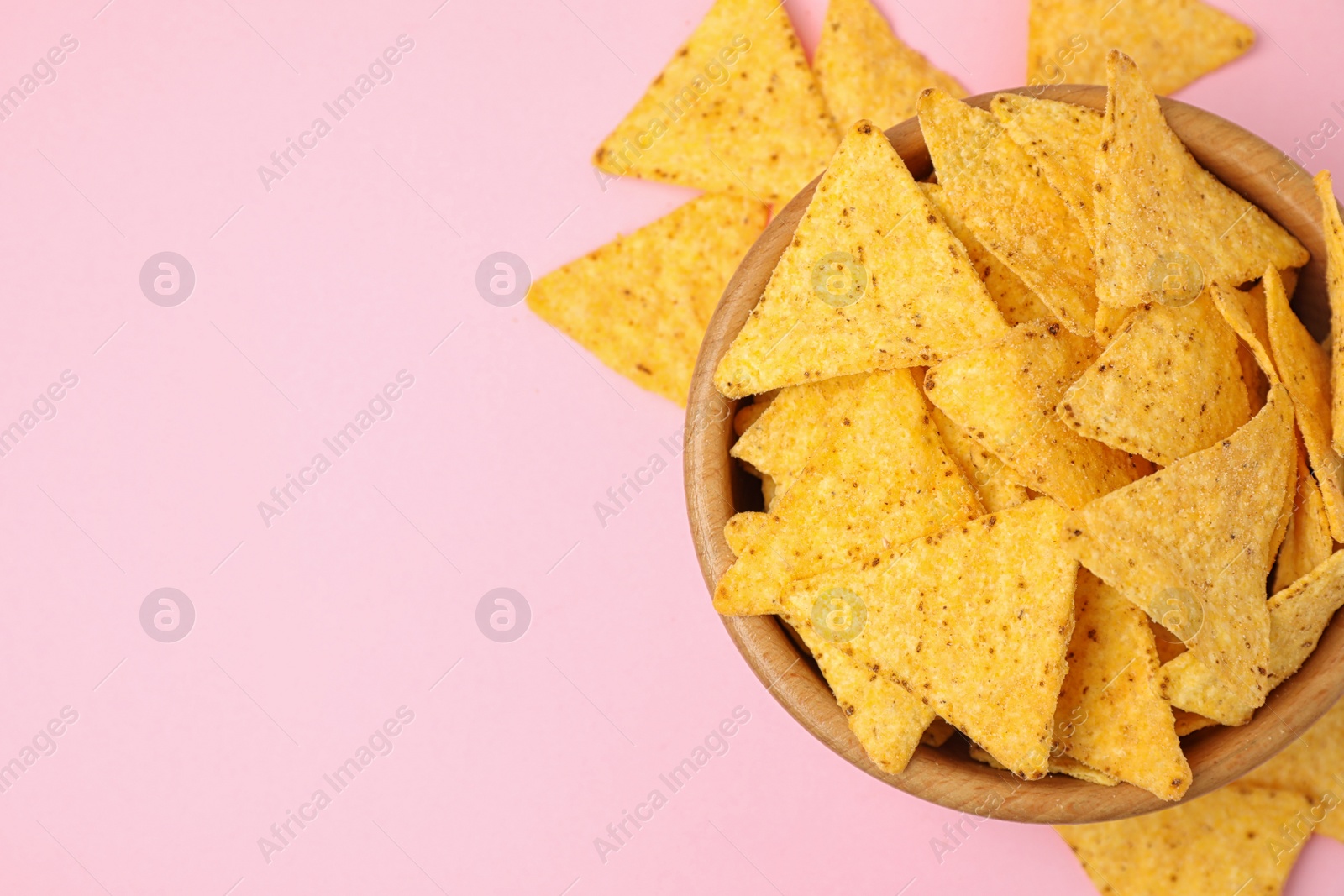 Photo of Wooden bowl with tasty Mexican nachos chips on pink background, flat lay. Space for text