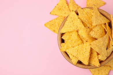 Wooden bowl with tasty Mexican nachos chips on pink background, flat lay. Space for text