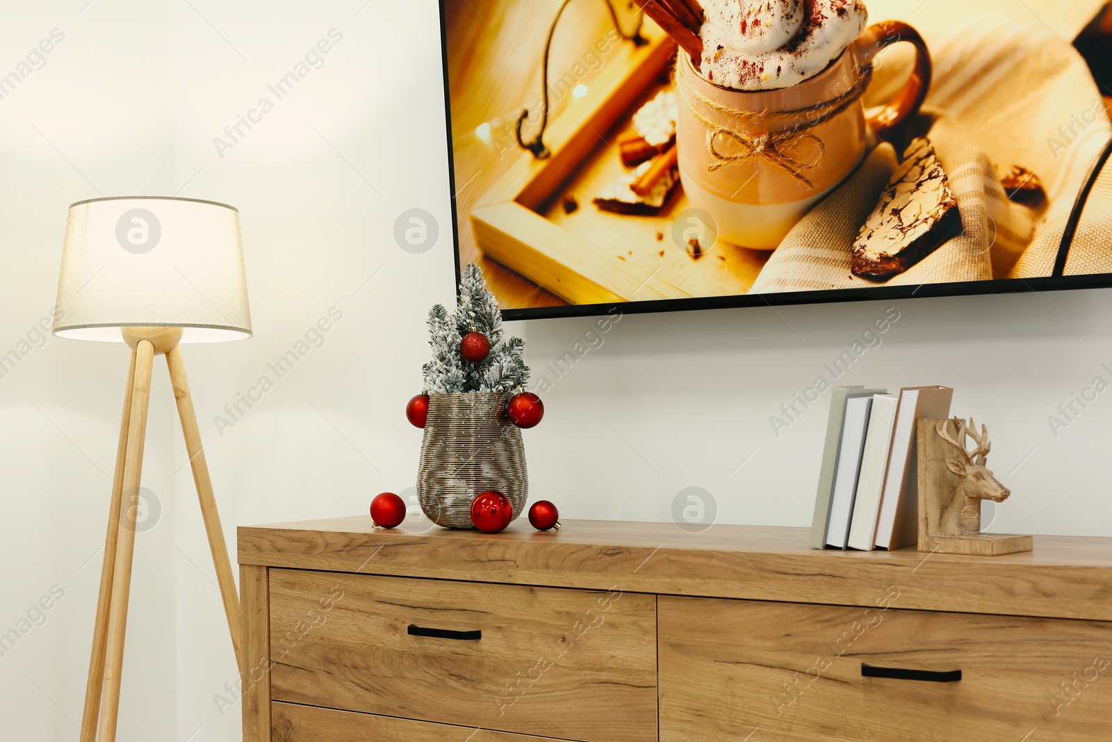 Photo of Wooden chest of drawers, stylish lamp and Christmas decor in room. Interior design