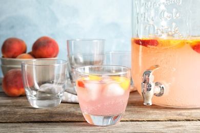 Photo of Peach cocktail in glass and jar with tap on table. Refreshing drink