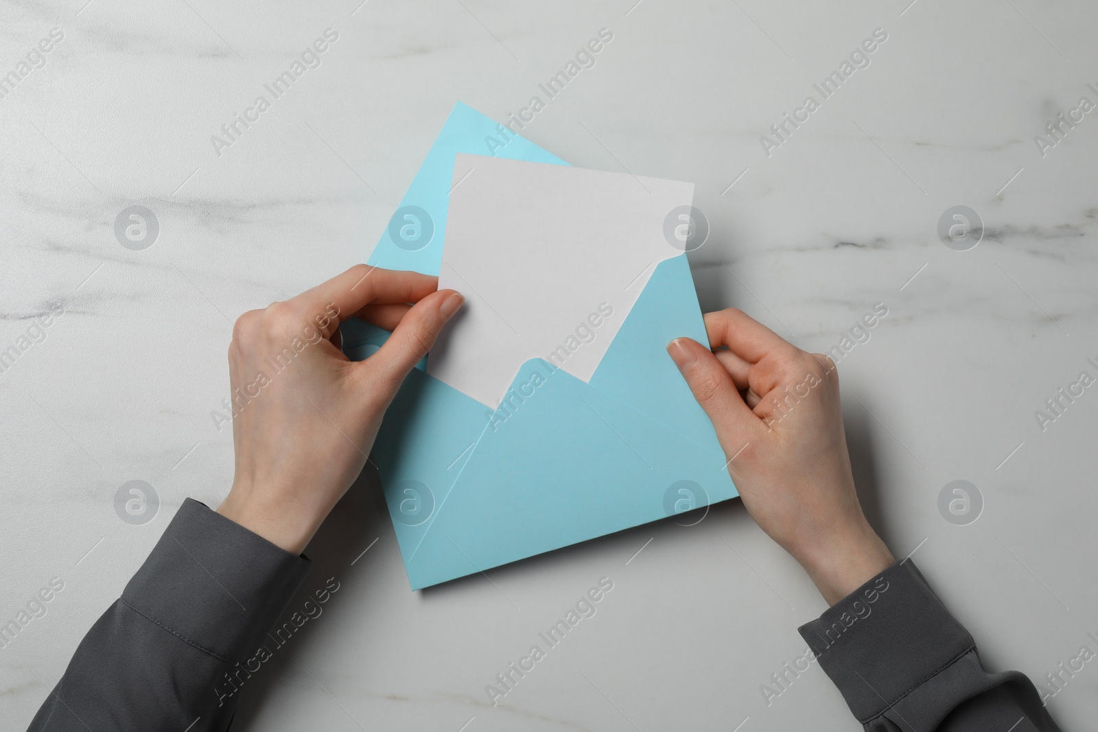 Photo of Woman taking card out of letter envelope at marble table, top view