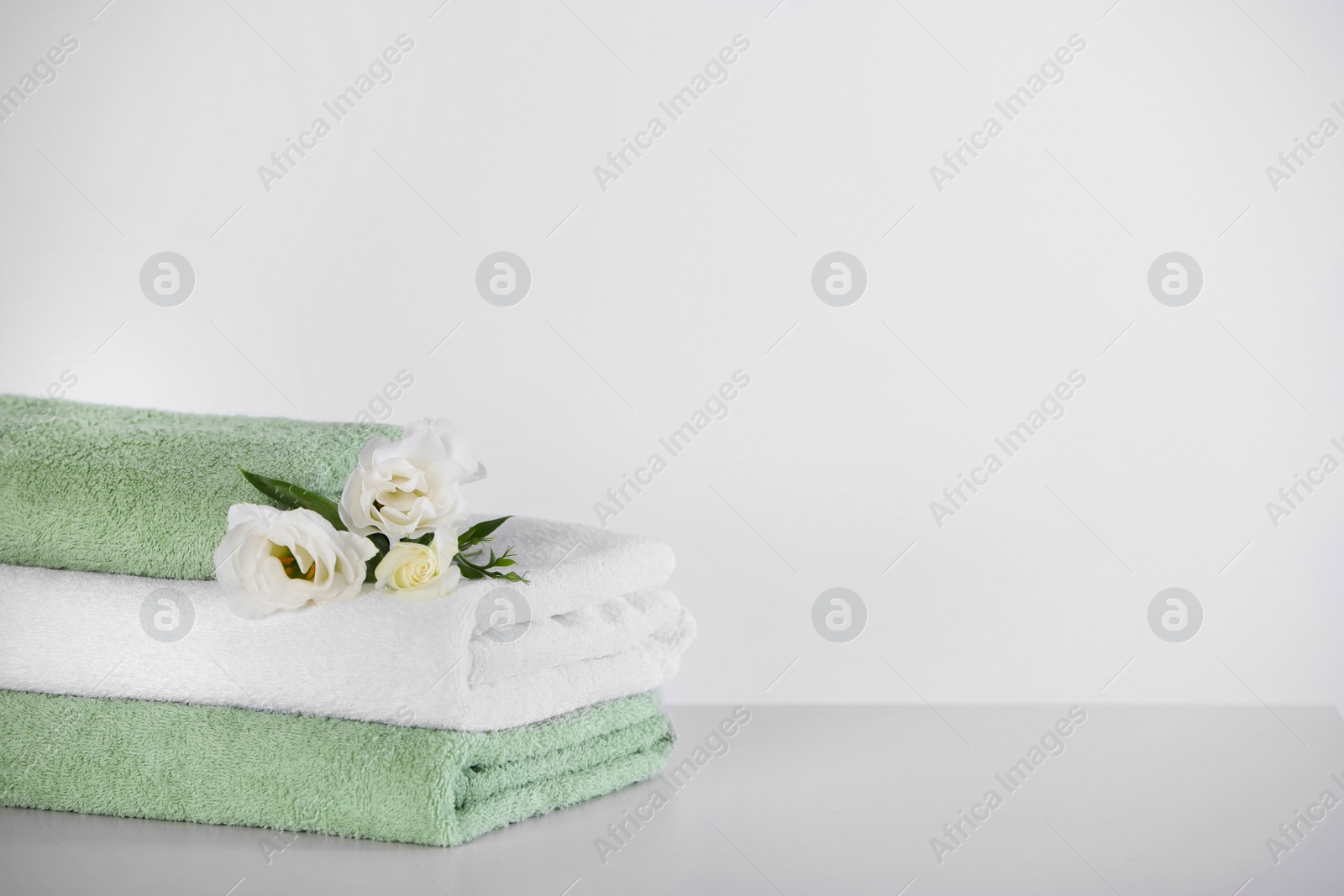 Photo of Soft folded towels with eustoma flowers on white table, space for text