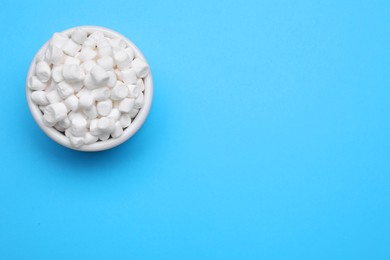 Bowl of sweet marshmallows on light blue background, top view. Space for text