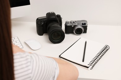 Photographer working at white table with cameras indoors, closeup