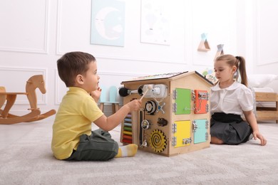 Little boy and girl playing with busy board house on floor in room