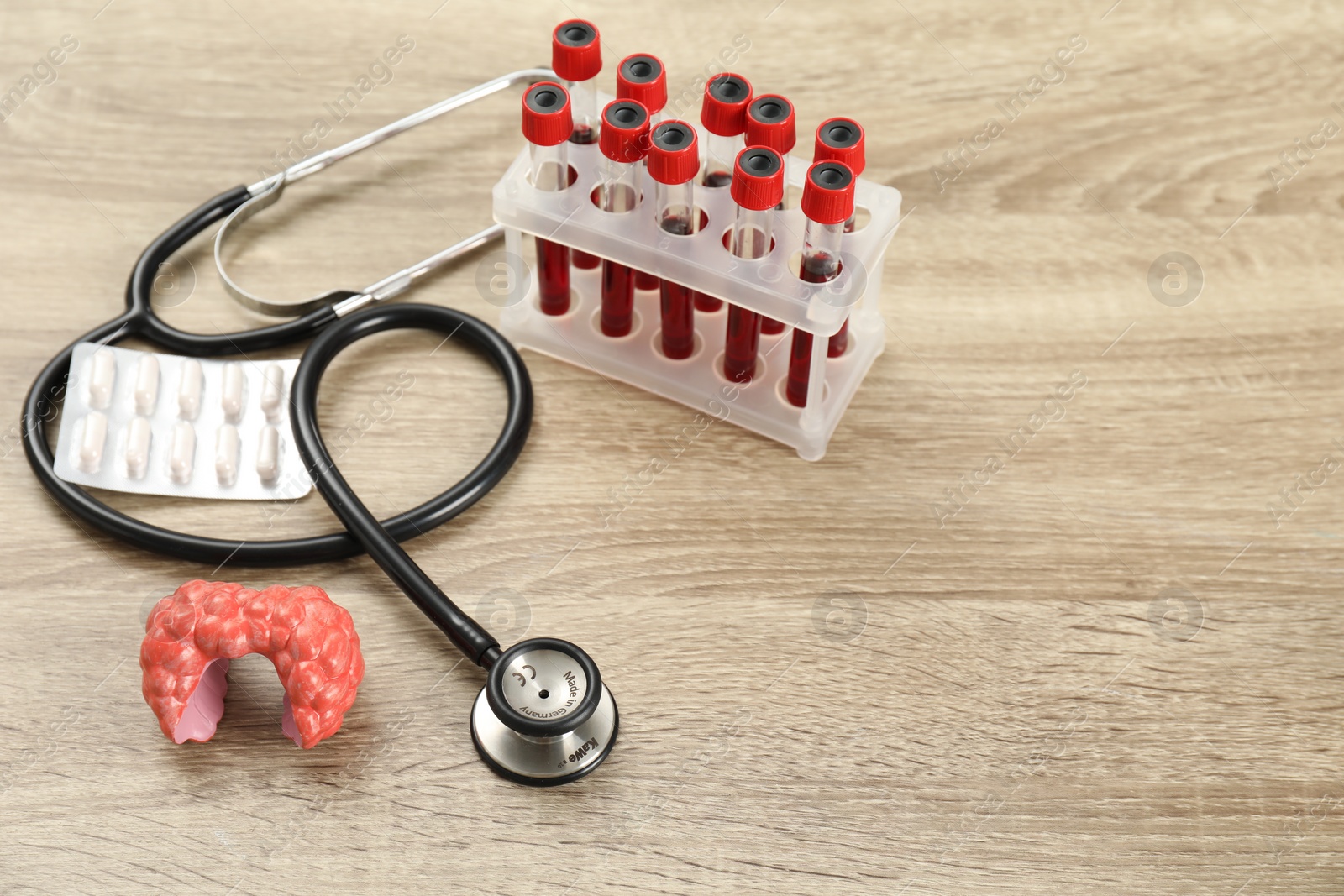 Photo of Endocrinology. Stethoscope, model of thyroid gland, pills and blood samples in test tubes on wooden table. Space for text