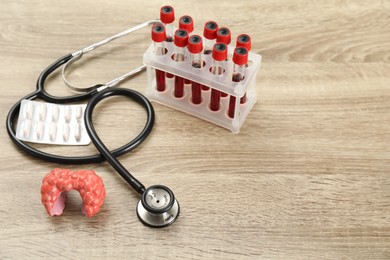 Endocrinology. Stethoscope, model of thyroid gland, pills and blood samples in test tubes on wooden table. Space for text