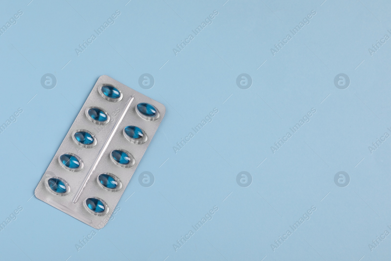 Photo of Pills in blister on light blue background, top view. Space for text