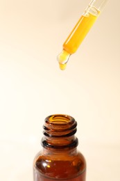 Dripping cosmetic serum from pipette into bottle on beige background, closeup